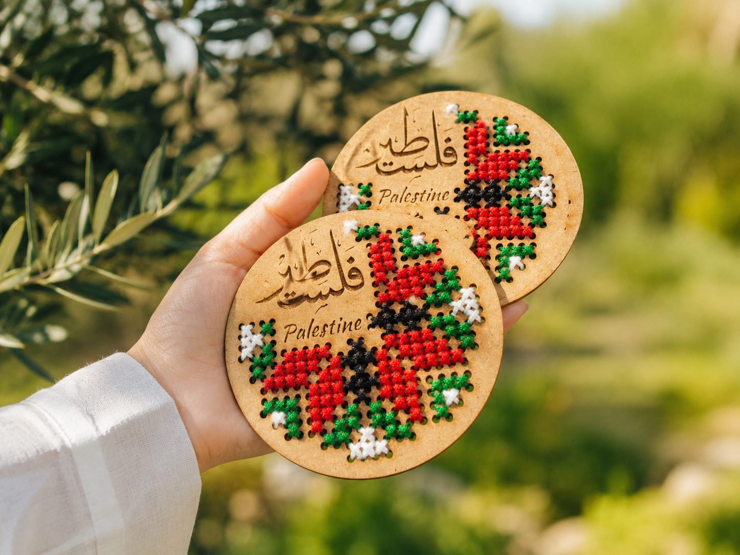 Handmade Palestine embroidery coasters held beneath an olive tree